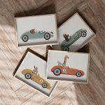 Printed set of four unframed wall art prints featuring animals (giraffe, bear, mole, rabbit) driving vintage race cars in orange, blue, green, and yellow colors. Perfect boys nursery or playroom decor.